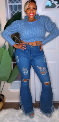 Person wearing a blue ribbed sweater and distressed jeans indoors.